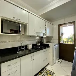 Foto interna de uma cozinha com armários brancos e bancada escura.