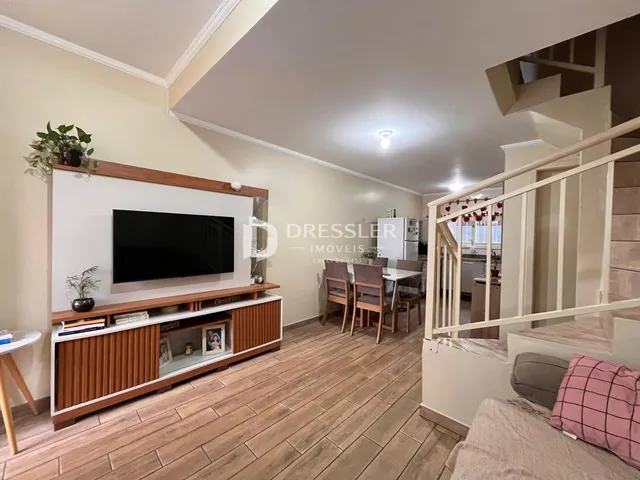 Sala de estar com piso de madeira e televisão montada na parede.