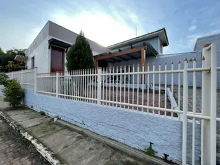 Fachada de uma residência em Lajeado, Brasil, com cerca branca e muro baixo.