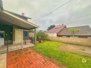 Vista da fachada de uma residência com quintal gramado e pátio de tijolos.
