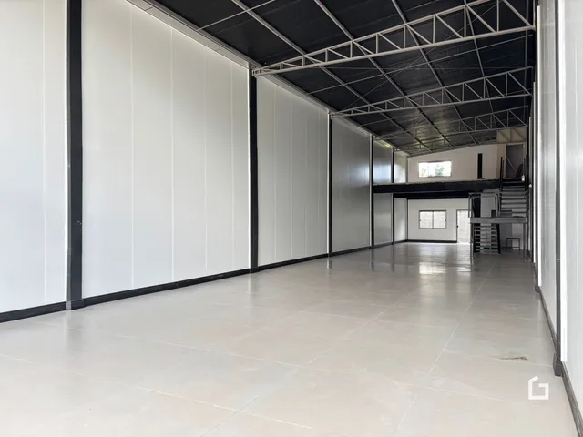 Corredor longo com paredes brancas e teto industrial.