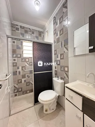 Banheiro com revestimento de azulejos e box de vidro, apresentando pia e vaso sanitário.
