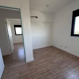 Vista interna de um cômodo com piso de madeira e paredes brancas.