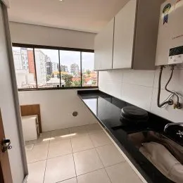 Vista interna de uma cozinha com armários brancos e grandes janelas.