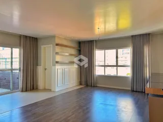 Sala de estar ampla com piso de madeira e grandes janelas.