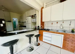 Vista interna de uma cozinha com armários brancos e parede de tijolos aparentes.
