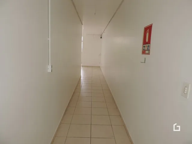 Corredor longo com piso de cerâmica claro e paredes brancas.