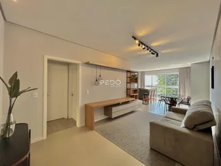 Sala de estar de um apartamento em Lajeado, Brasil, com piso de madeira clara e grande janela.