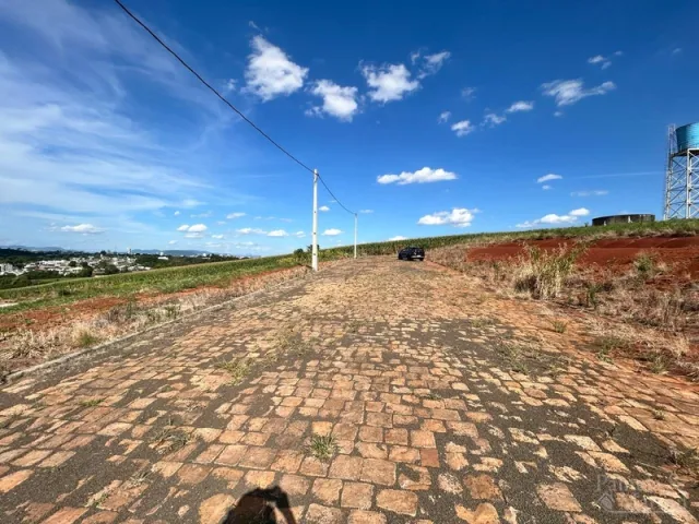 Vista de uma estrada de terra sob um céu azul com nuvens no exterior de uma propriedade.