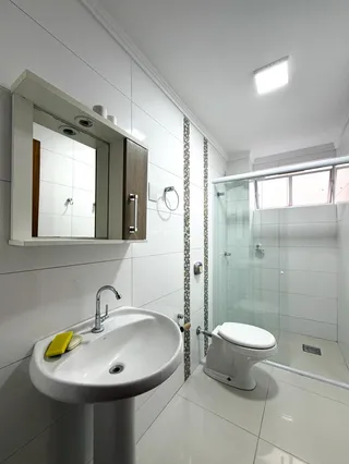 Banheiro moderno com piso de cerâmica e box de vidro transparente.