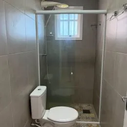Foto interna de um banheiro com box de vidro e vaso sanitário.