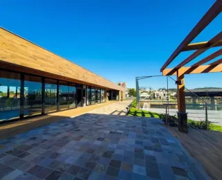 Vista externa de uma residência moderna com grandes painéis de vidro e área de piso pavimentado.