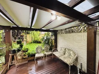 Uma varanda de madeira com móveis está voltada para um jardim verde.