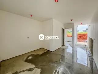 Foto de um ambiente interno com piso de concreto cru e paredes brancas em construção.
