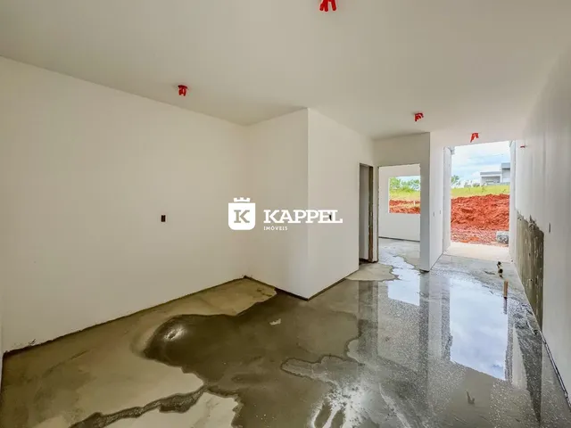 Foto de um ambiente interno com piso de concreto cru e paredes brancas em construção.