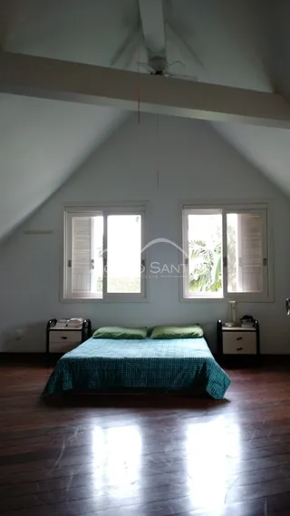 Quarto com cama de casal e janelas em ambiente com teto inclinado.