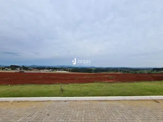 Paisagem de campo com terra vermelha e grama verde sob um céu nublado.