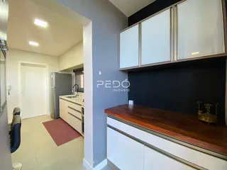 Vista interna de uma cozinha com armários brancos e bancada de madeira escura.