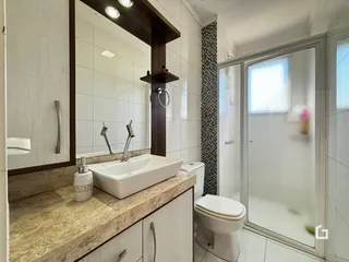 Imagem de um banheiro com revestimento cerâmico e box de vidro.