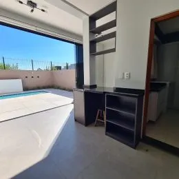 Vista de uma área externa com piscina visível através de uma grande abertura no ambiente interno.