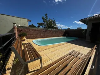 Vista externa de uma piscina e área de lazer com muro de tijolos.