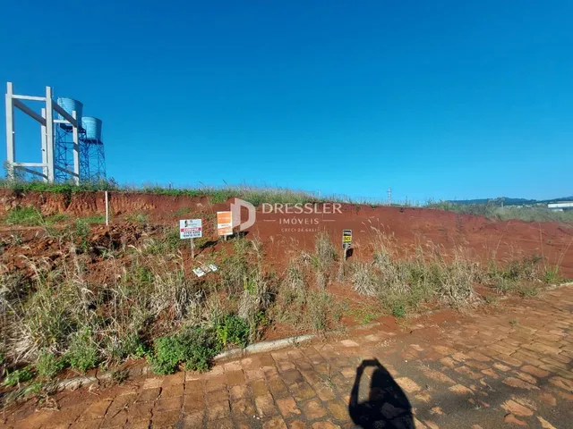 Vista de uma área de terra com vegetação seca e uma estrutura metálica ao fundo.