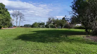 Vista de um campo gramado com árvores ao fundo sob um céu parcialmente nublado.