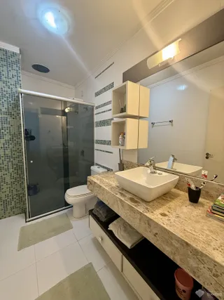 Foto de um banheiro com box de vidro e bancada de granito.