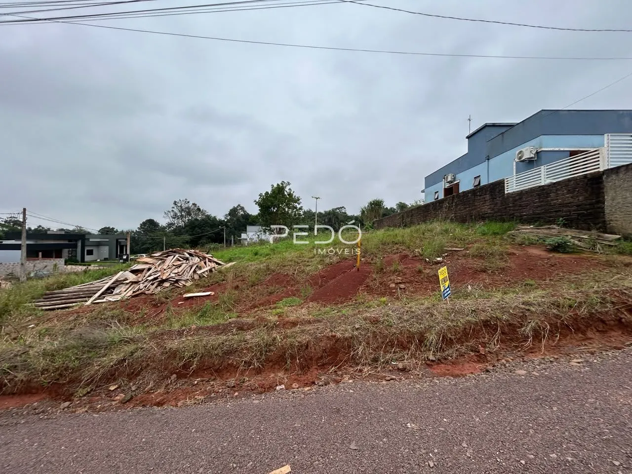 Vista externa de uma propriedade com terra e vegetação ao lado de uma estrada.