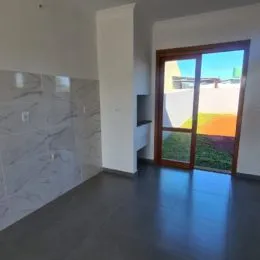 Sala de estar com piso escuro e porta de vidro que dá acesso a uma área externa.