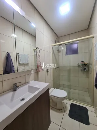 Interior de um banheiro com revestimento cerâmico e box de vidro transparente.