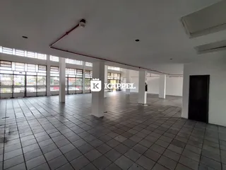 Vista interna de um grande hall com piso de cerâmica e colunas brancas.