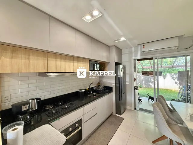 Cozinha moderna com armários brancos e bancadas escuras, com vista para o jardim externo.