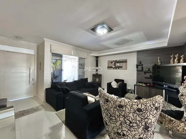 Sala de estar com sofá e poltronas escuras e piso de cerâmica clara.