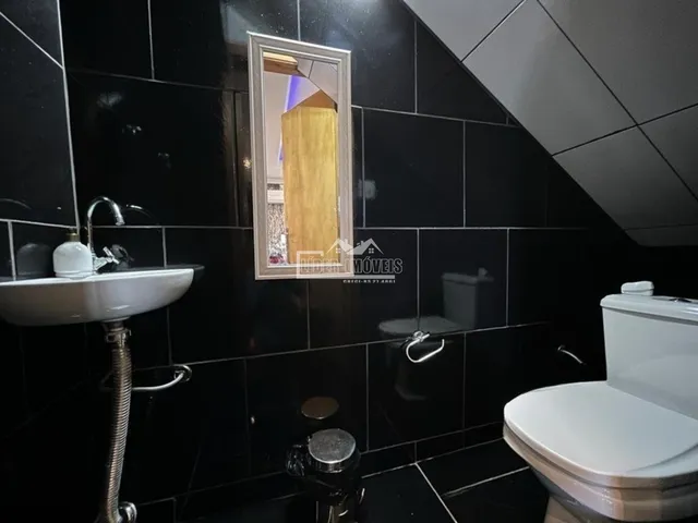 Banheiro com revestimento de azulejos escuros e louças sanitárias brancas.