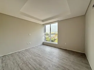 Ambiente interno de uma sala com piso de madeira clara e grande janela.