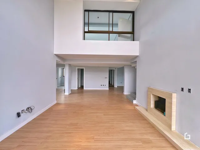 Vista de um hall interno com piso de madeira clara e parede branca.