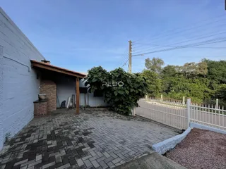 Fachada da propriedade com pátio pavimentado e vegetação ao fundo.