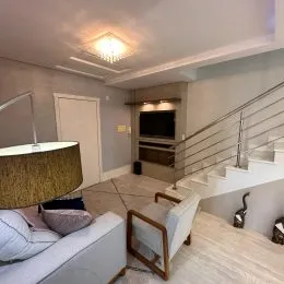 Imagem interna mostrando uma área de estar com sofá e escadaria.