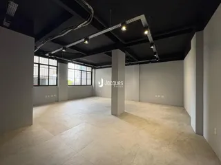 Vista interna de um espaço amplo com piso de concreto polido e grandes janelas.