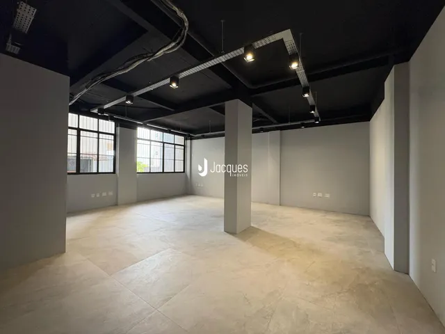 Vista interna de um espaço amplo com piso de concreto polido e grandes janelas.