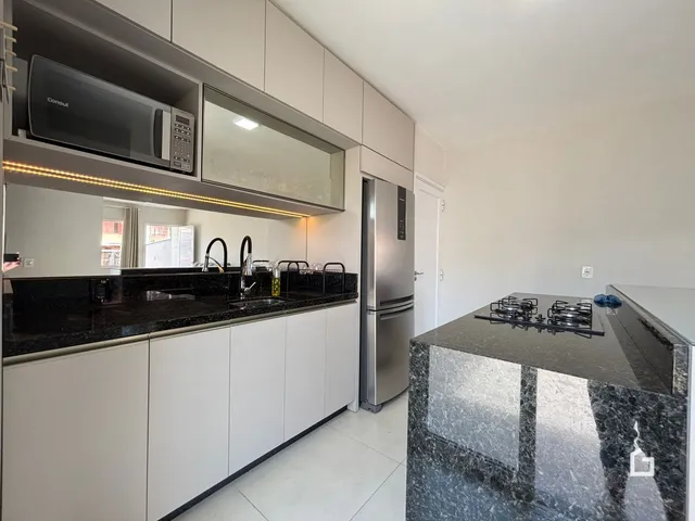 Foto de uma cozinha moderna com armários brancos e bancadas escuras.