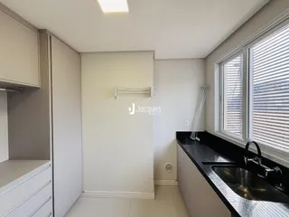 Vista interna de uma cozinha com armários brancos e bancada escura.