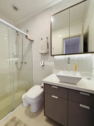 Banheiro com box de vidro, vaso sanitário e bancada de pia.