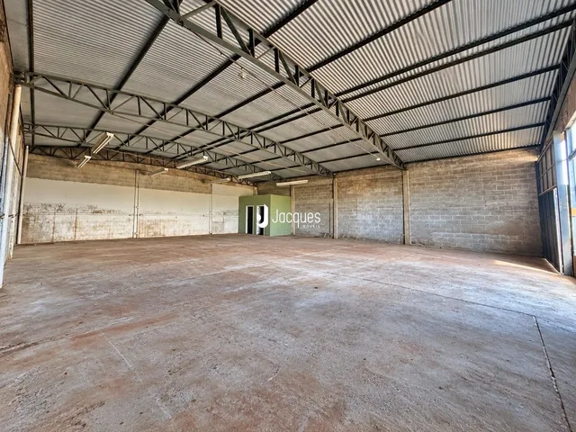 Espaço interno amplo com estrutura de telhado metálico e paredes de concreto.