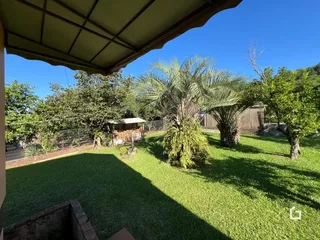 Vista de um jardim gramado com árvores sob um céu azul.