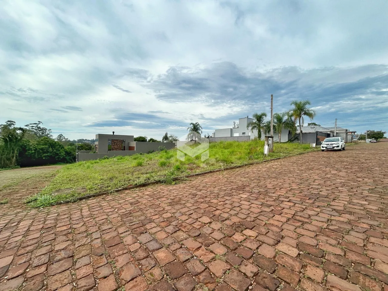 Vista externa de uma propriedade com terreno gramado e pavimentação de tijolos.