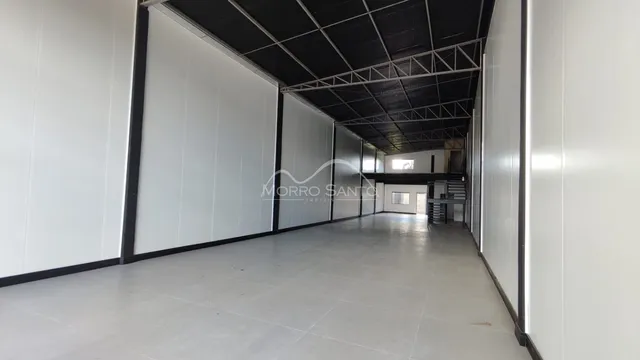 Hall de passagem com paredes brancas e teto estrutural exposto.