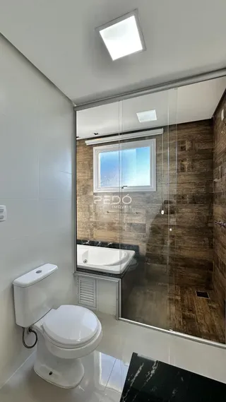 Interior de um banheiro com revestimento branco e vidro separando o box.