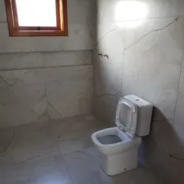 Foto de um banheiro com revestimento de azulejos claros e um vaso sanitário branco.